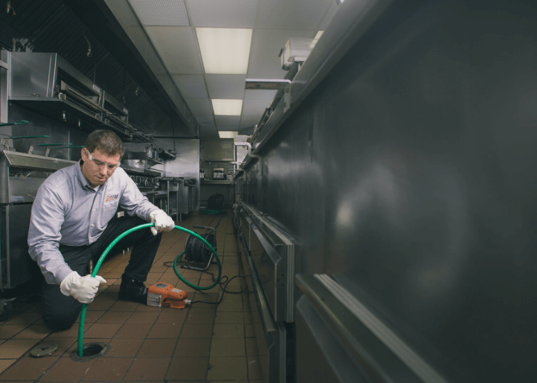 A Zoom Drain specialist holds a hose down a commercial kitchen drain