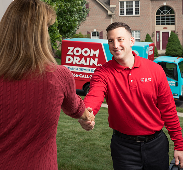 A Zoom Drain specialist shakes hands with a woman in front of a house