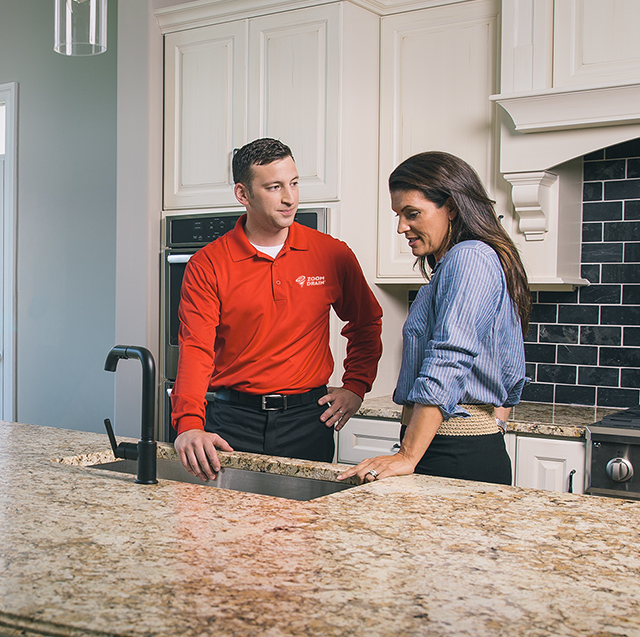 A Zoom Drain technician and a woman stand in front of a kitchen sink