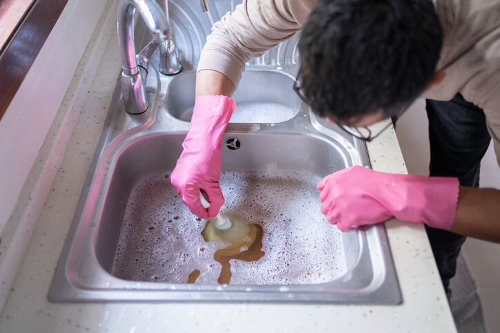 Man Using Plunger on clogged Kitchen Sink.
